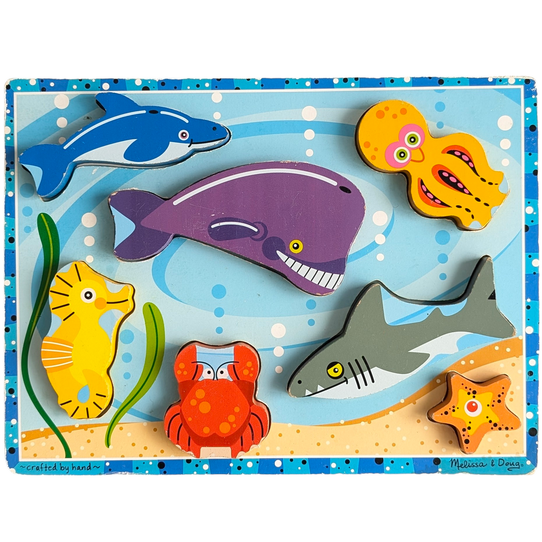 Melissa & Doug, Sea Creatures Chunky Puzzle, Cognitive & Motor Skills Development, Melissa and Doug's chunky sea creature puzzle. Big wooden pieces indicate creative play. Puzzle board with seven pieces and picture underneath the pieces. This extra-thick wooden puzzle features seven easily graspable aquatic creatures, including an octopus, shark, and whale. For pretend play, the hefty pieces with corresponding full-color pictures underneath can be lifted out of the depths.